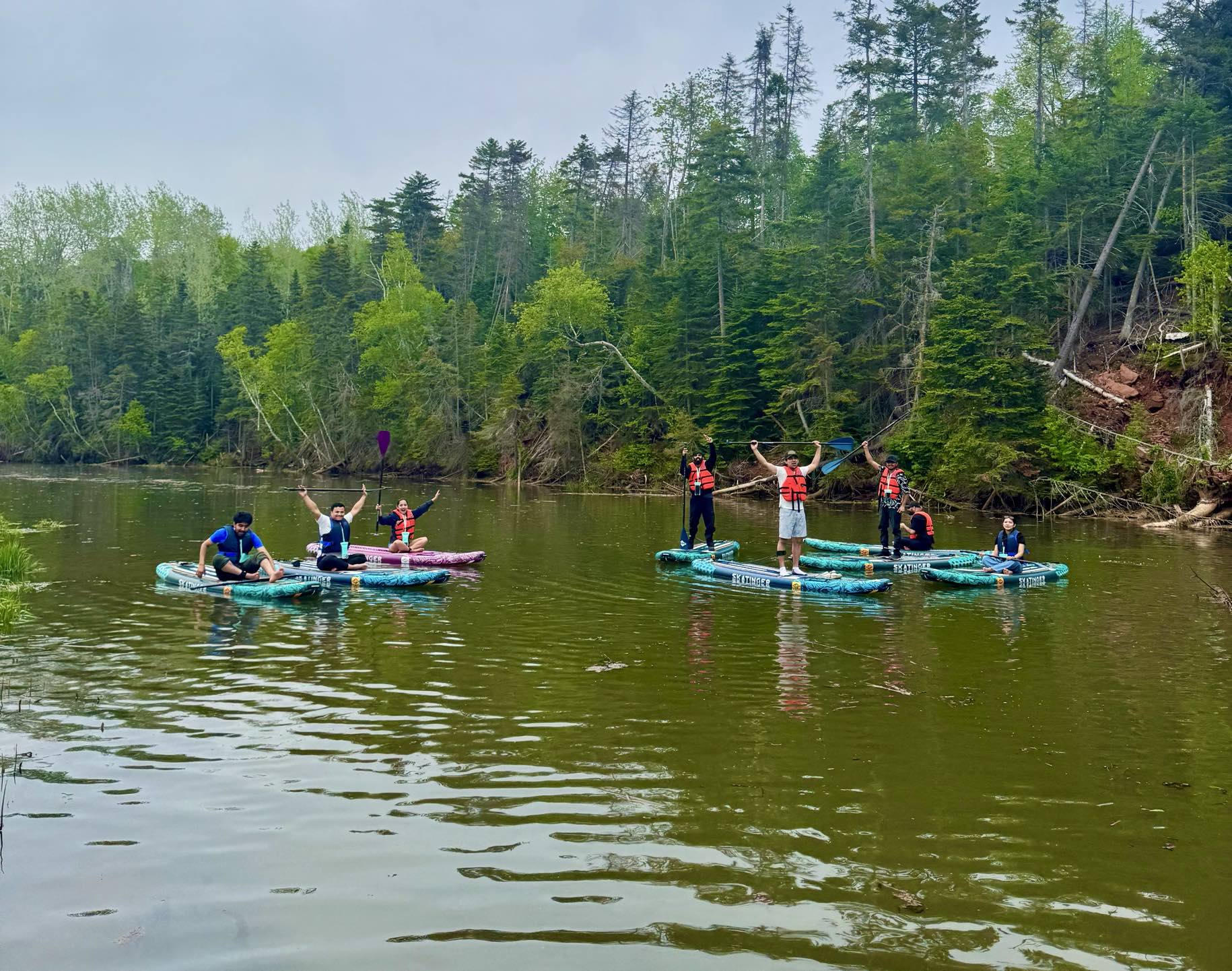 Group paddleboarding on a forest-lined river with premium inflatable boards