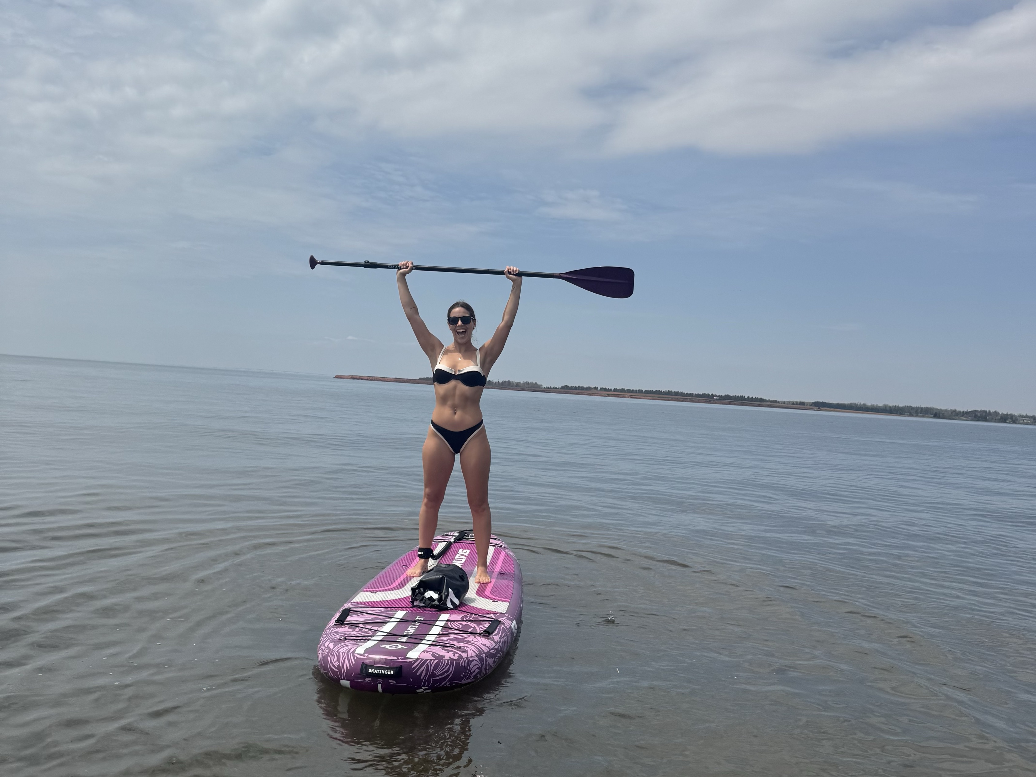 Woman celebrating with her paddle raised overhead while standing on an inflatable paddle board