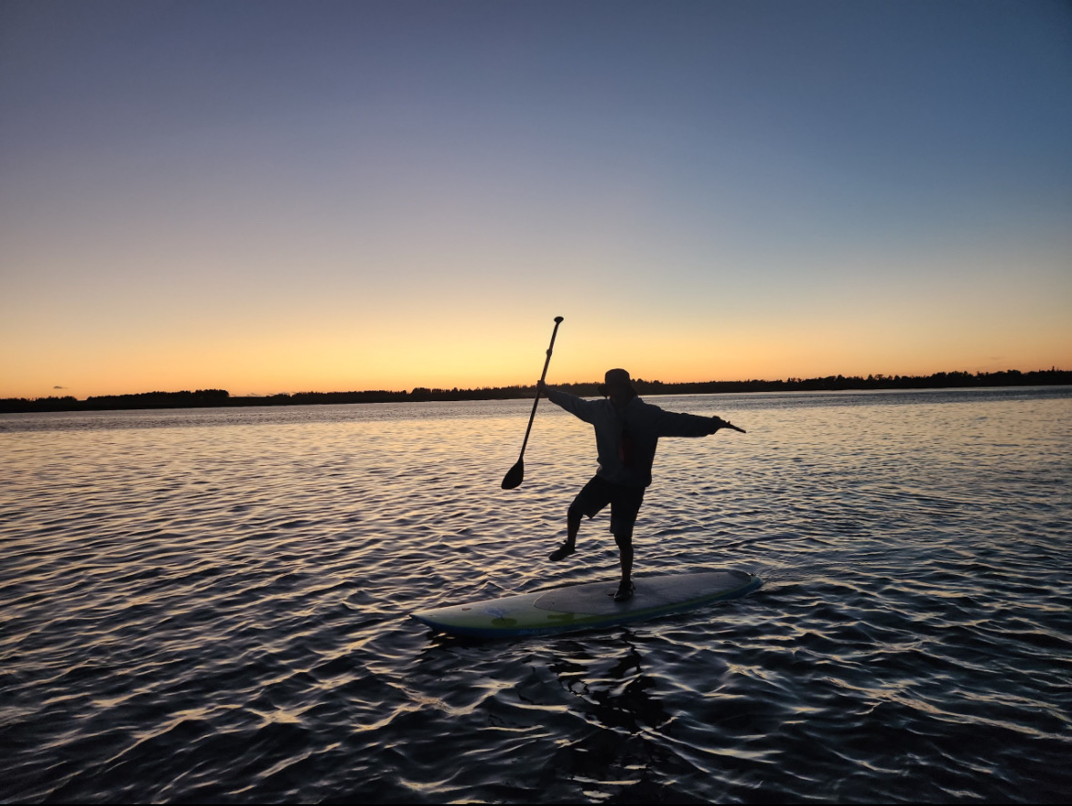 Paddler balancing on a board in silhouette against a vibrant orange sunset