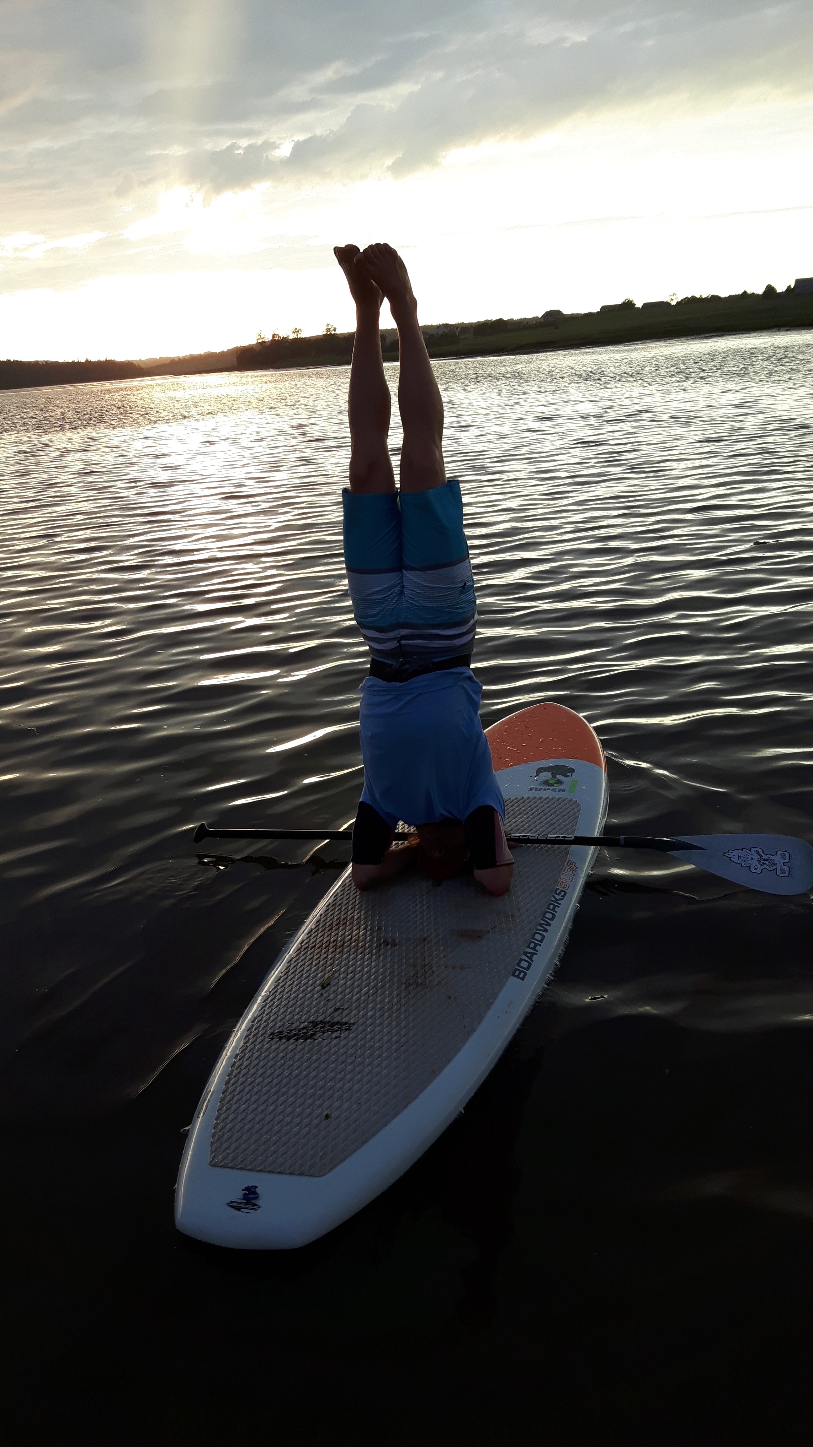 Person doing a headstand on a paddleboard at sunset, representing flexible rentals